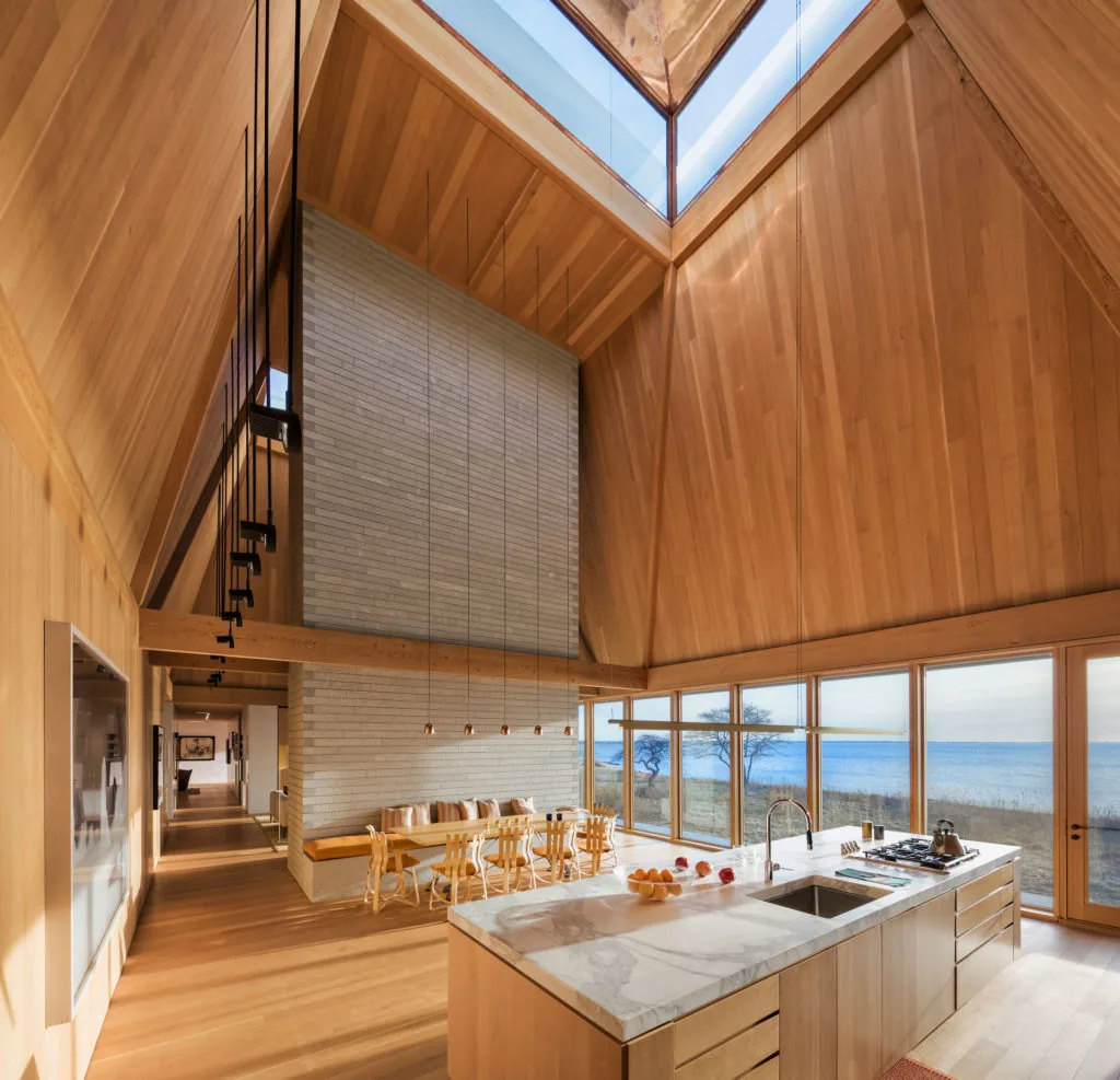 Interior view of the kitchen and dining area with wood finishes, a skylight, and large windows overlooking a water view.