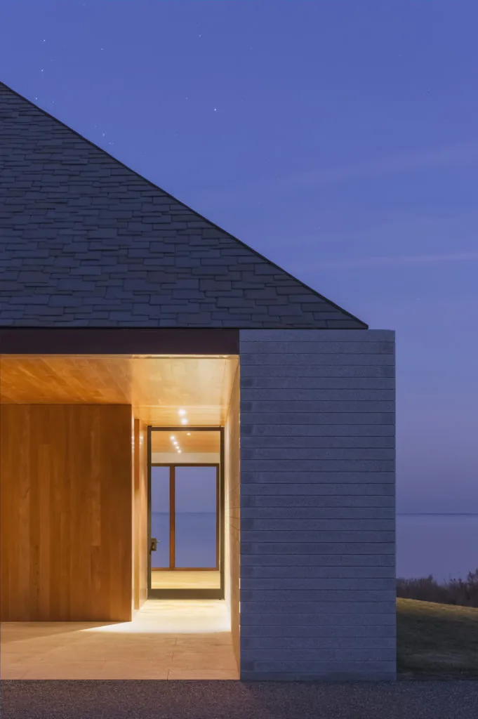 Entrance of the Bayhouse at dusk, showing wood-paneled interior and stone exterior walls with a gable roof above.