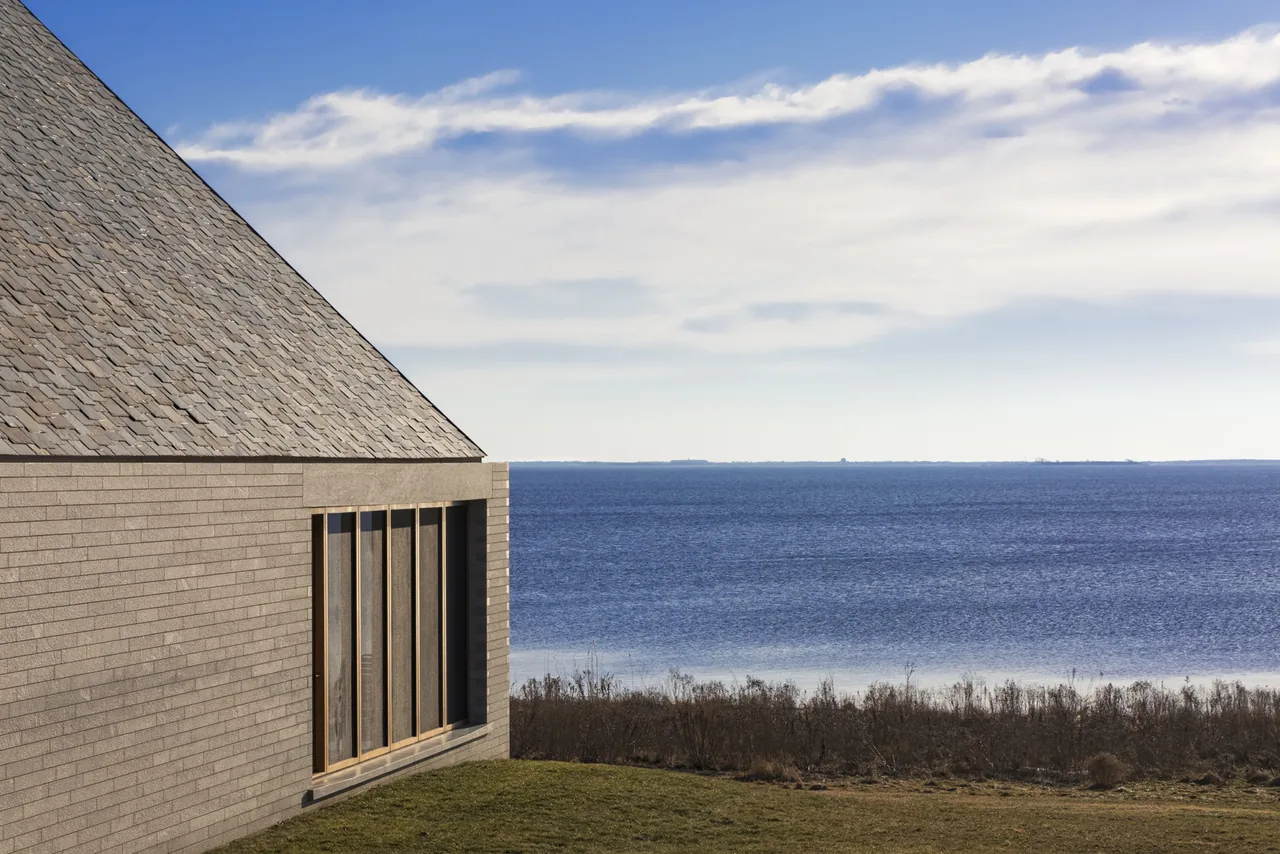 Exterior side view of a brick house with slate roofing next to a waterfront landscape.