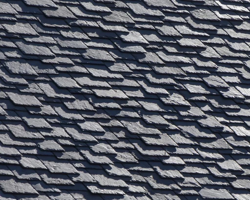 Detail of dark gray slate tiles on a roof with visible shadows.