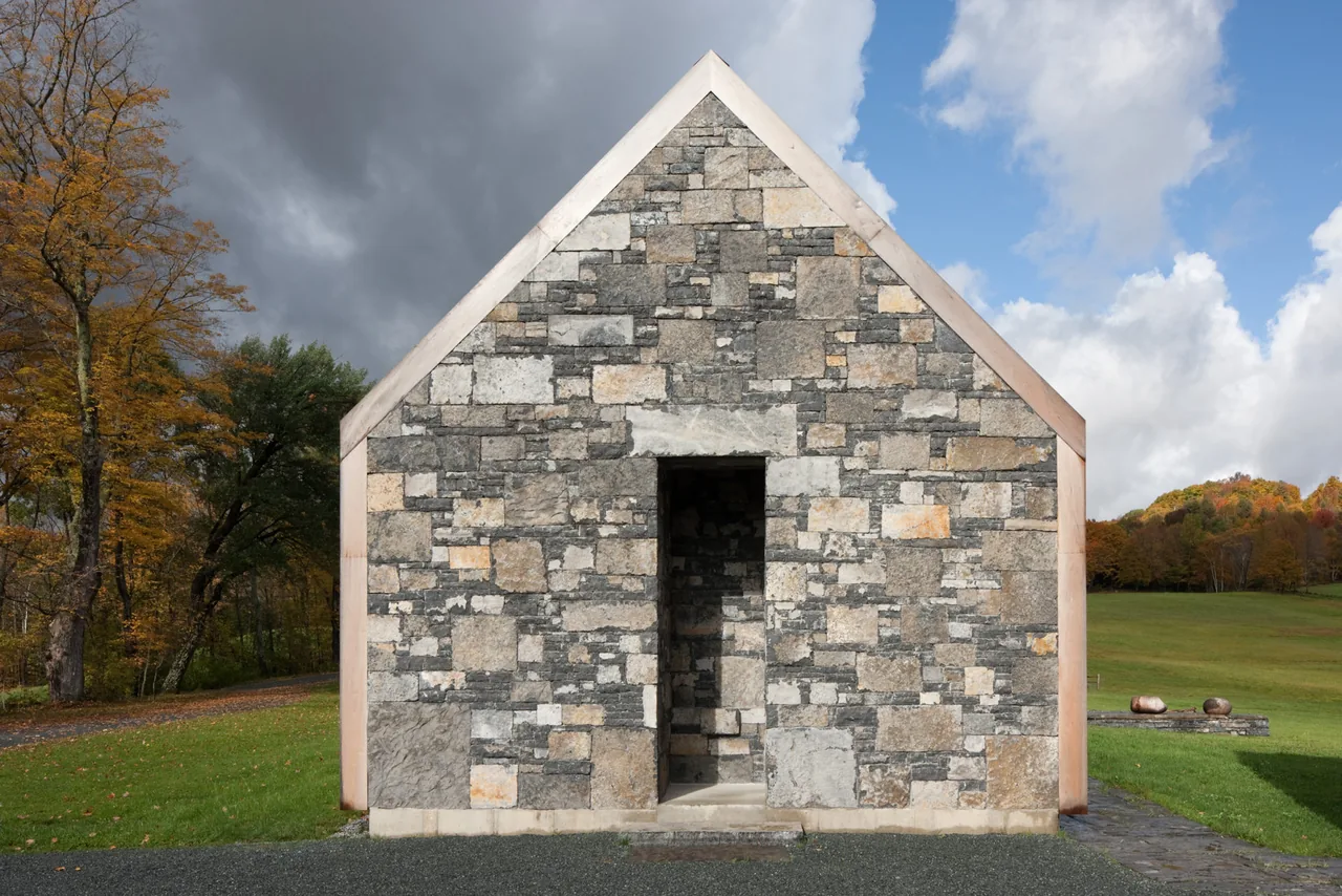 The front facade of a small stone building features a centered entrance and a steep gable roof with copper edging.