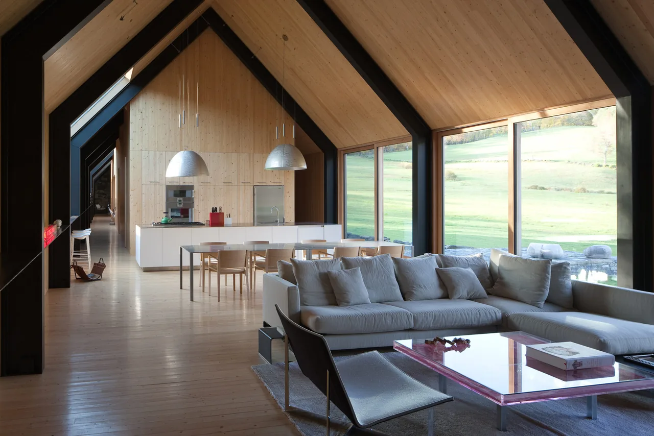 Open living and dining area under a vaulted wood-paneled ceiling with floor-to-ceiling windows.