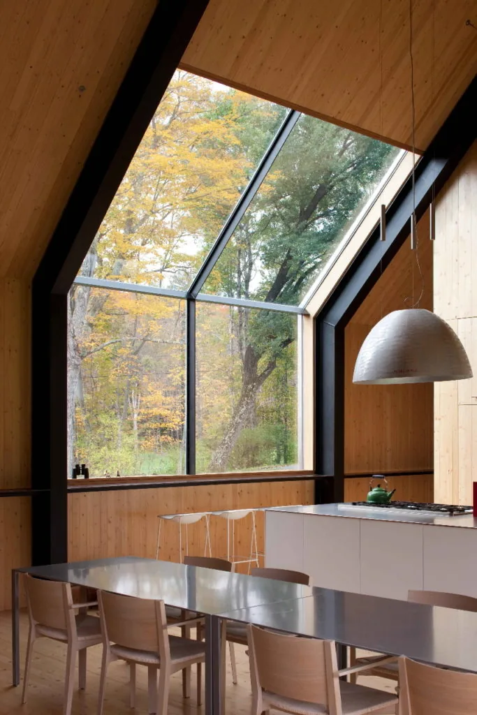 Kitchen and dining area with floor-to-ceiling corner windows and wood-paneled vaulted ceiling.