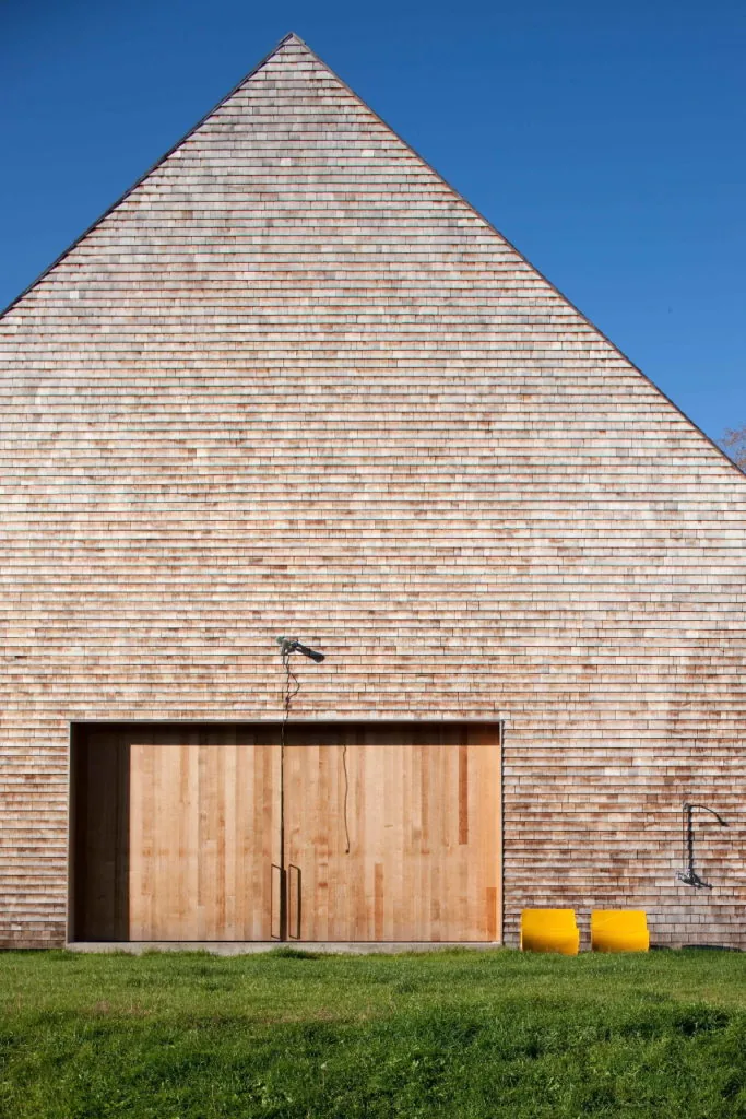 A gable-roofed structure with wooden shingle siding and a large sliding wood door.