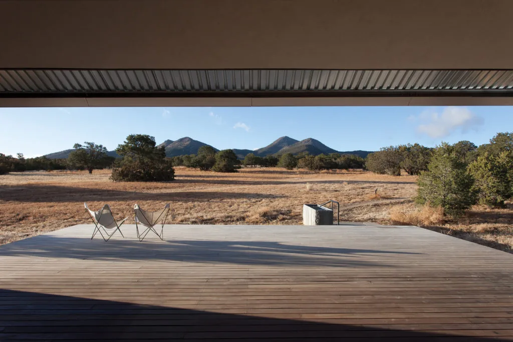 Wooden deck with two chairs overlooking a rural landscape and distant mountains.