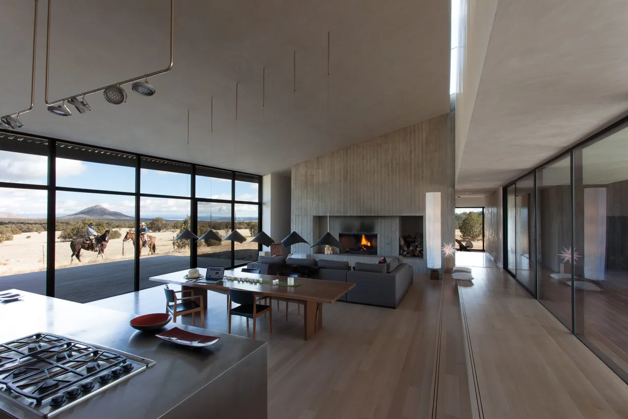 Open living and kitchen area featuring floor-to-ceiling glass walls, a concrete fireplace, and vaulted ceiling.