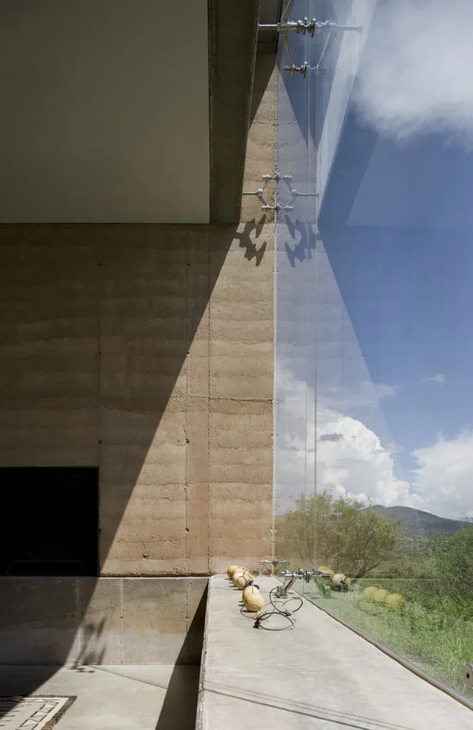 Rammed earth wall meets floor-to-ceiling glass window with landscape and mountain views.