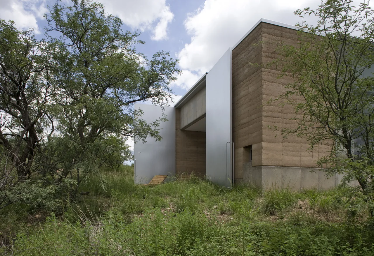 The Adobe Canyon House features rammed earth walls combined with smooth metal panels in a natural setting.