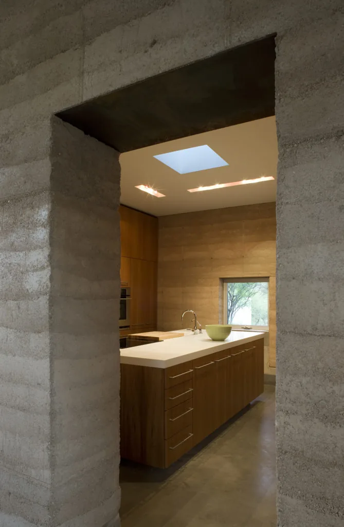 Kitchen featuring rammed earth walls, a skylight, and wooden cabinetry with a central island.