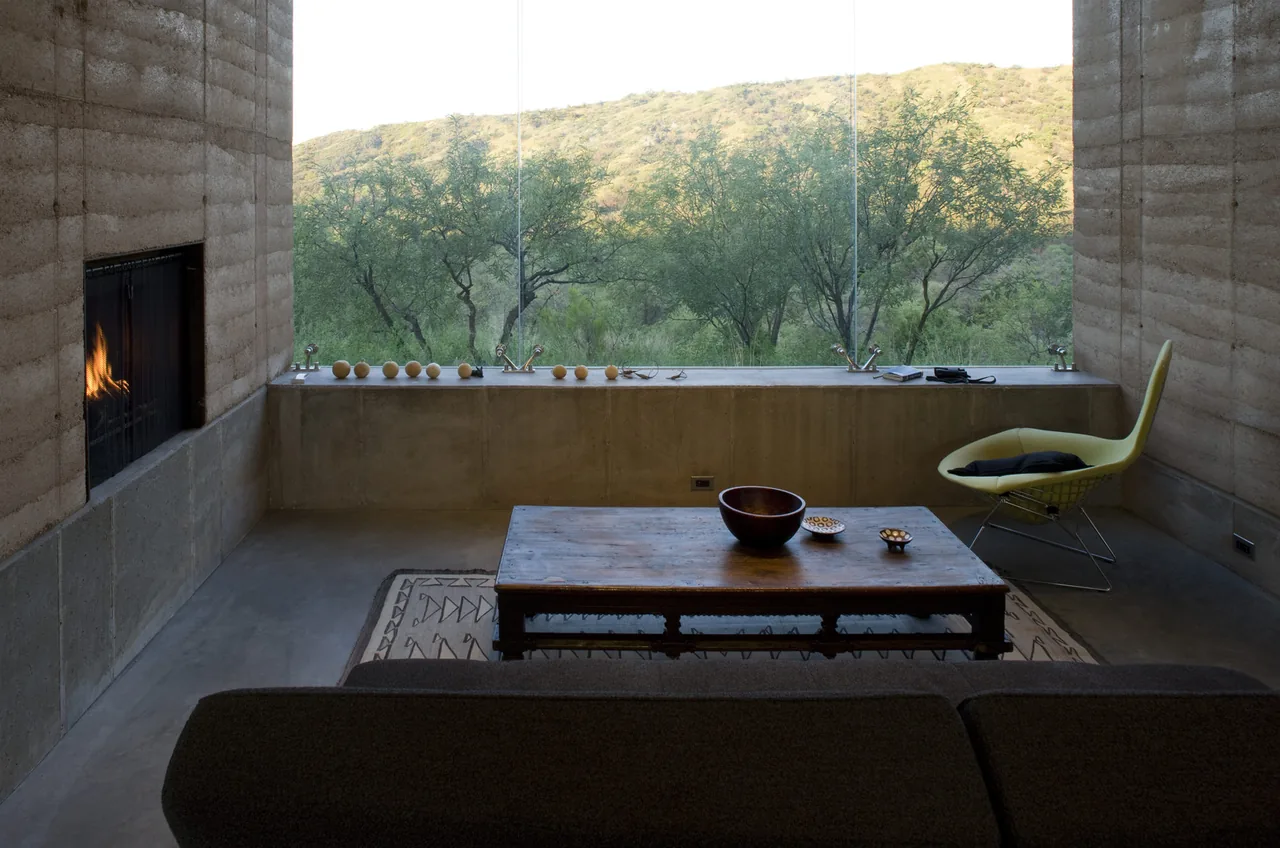 Living room with rammed earth walls, concrete floor, and a large picture window overlooking vegetation.