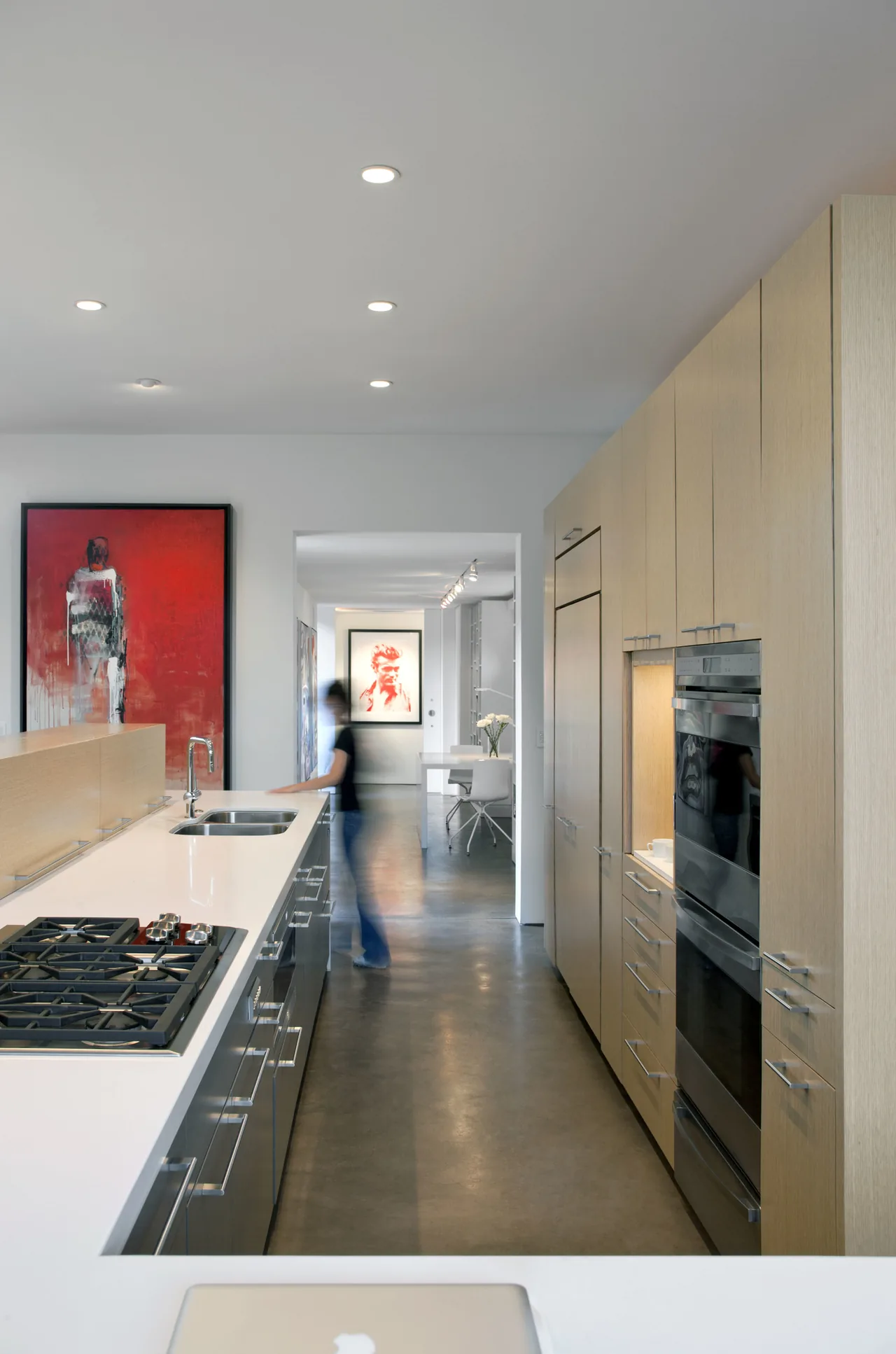 This modern kitchen features a sleek white island with a gas cooktop and sink, alongside light wood cabinets and stainless steel appliances.
