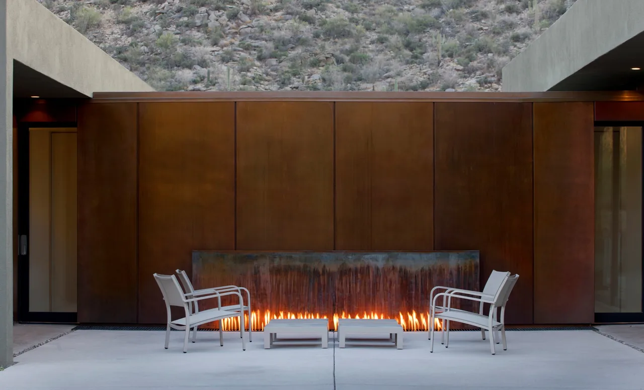 Outdoor patio with rusted steel fire feature and white seating furniture overlooking desert terrain.