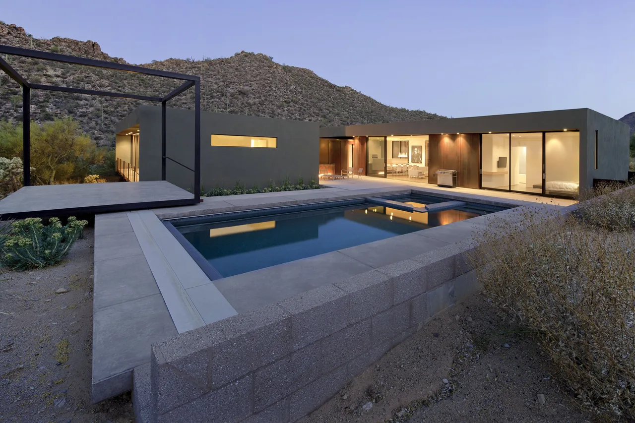 Modern house with flat roof and large sliding glass doors opening to pool area and mountain views.
