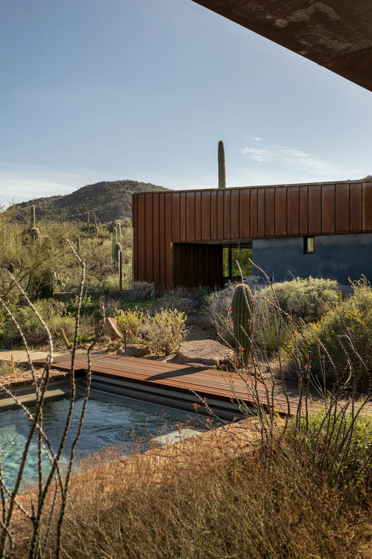 The TS Falls West Residence features rust-colored metal paneling and desert landscaping with a reflective pool, designed by Ibarra Rosano Design Architects.