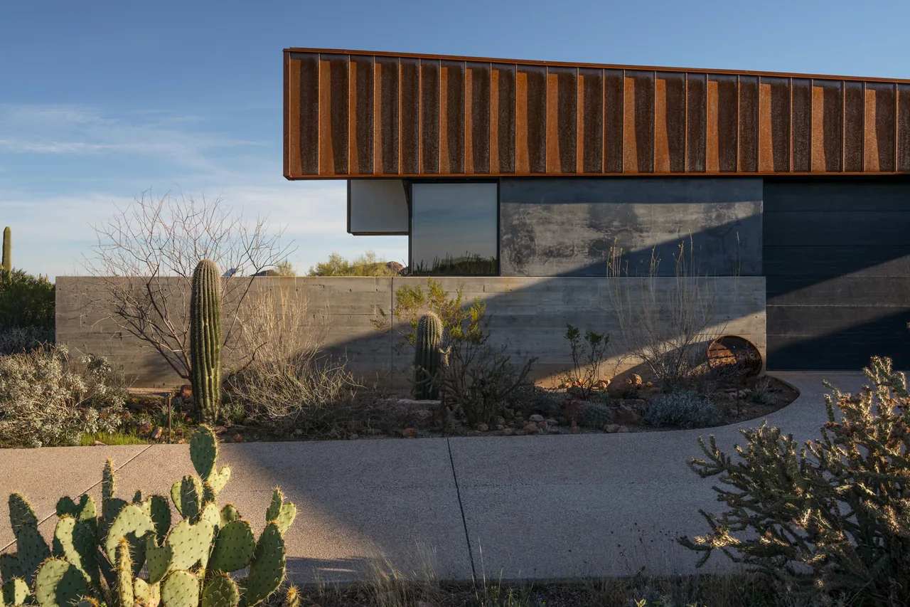 TS Falls West Residence features rust-colored metal panels and concrete walls with a desert landscape including cacti in front.