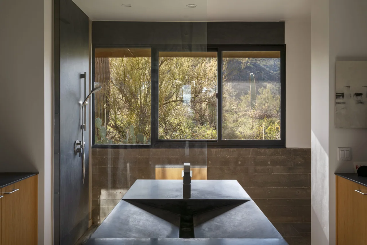 Bathroom features a wide window framing desert plants and distant mountains with a dark stone sink in the foreground.