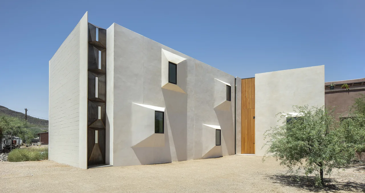 Exterior front view of a modern house with beige stucco walls and angular window projections under a clear blue sky.
