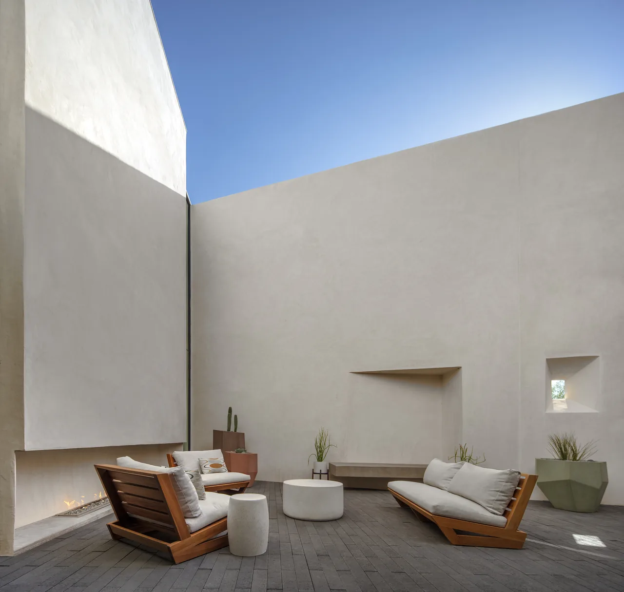 Outdoor courtyard with stucco walls, wooden lounge seating, and a linear built-in fireplace in Casa Schneider.