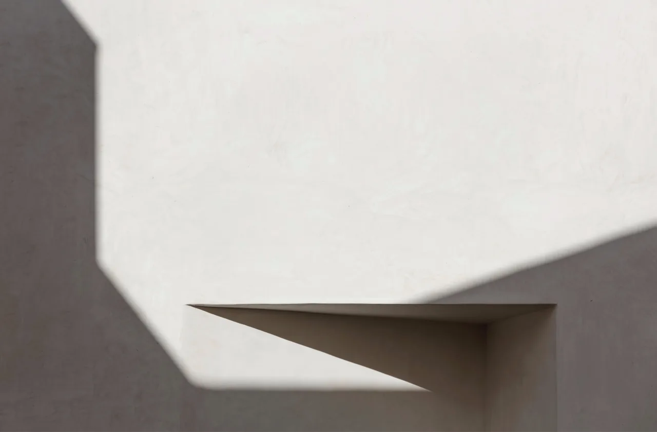 Shadow and light on a white plaster wall with an angular shadow formed by a deep rectangular recess.