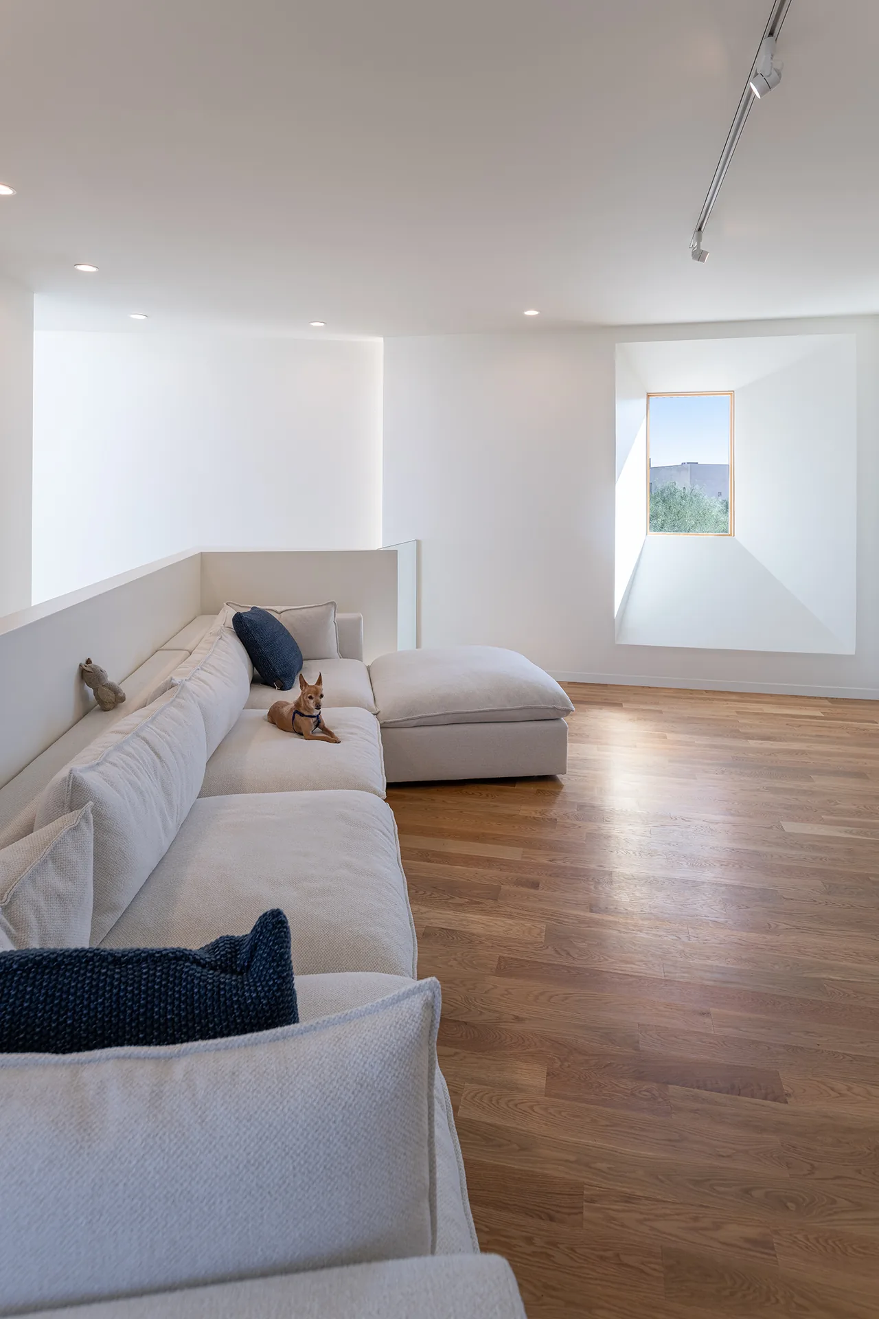 Living room in Casa Schneider features a white sectional sofa, wood flooring, and a deep wall recessed window with natural light.