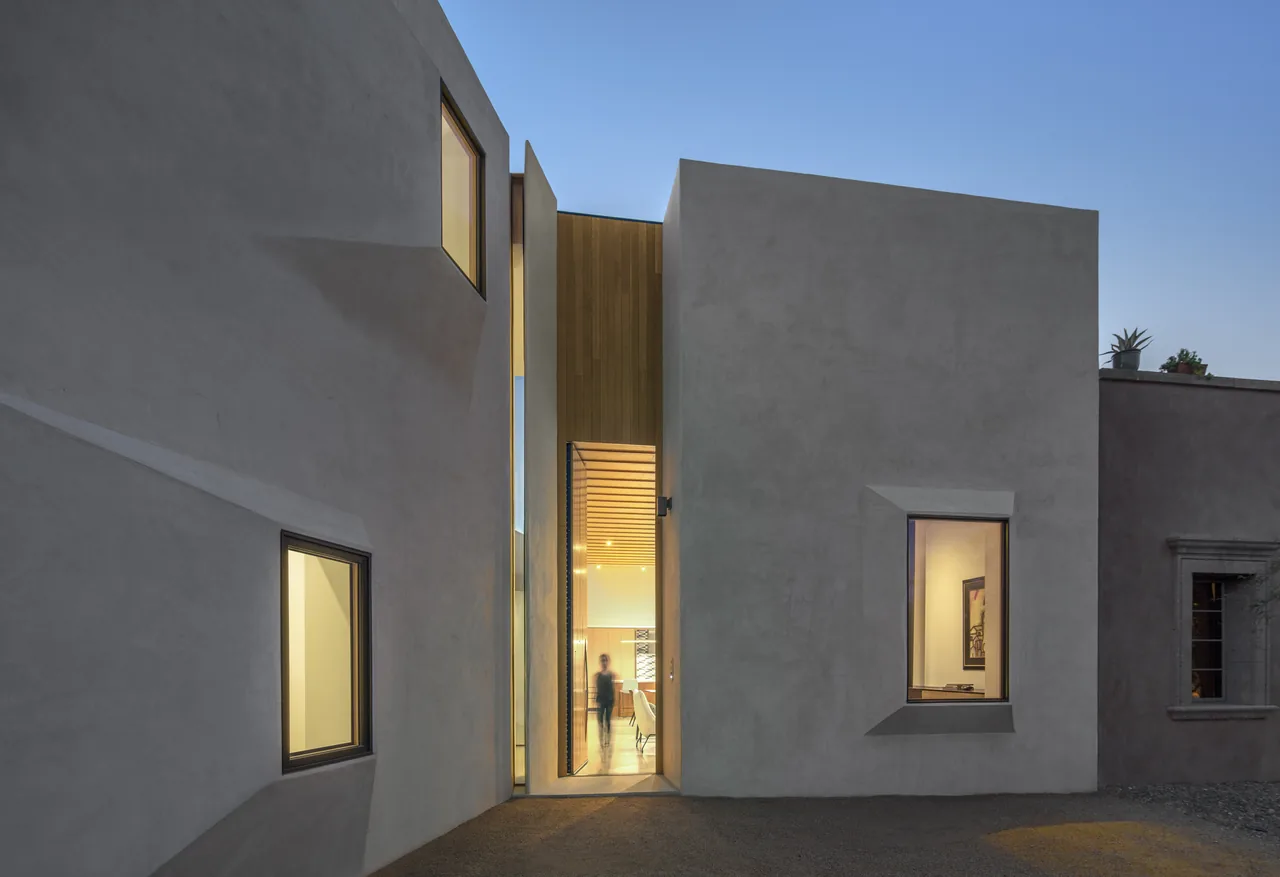 Casa Schneider features a white stucco exterior with angular window frames and a tall wooden entry door.