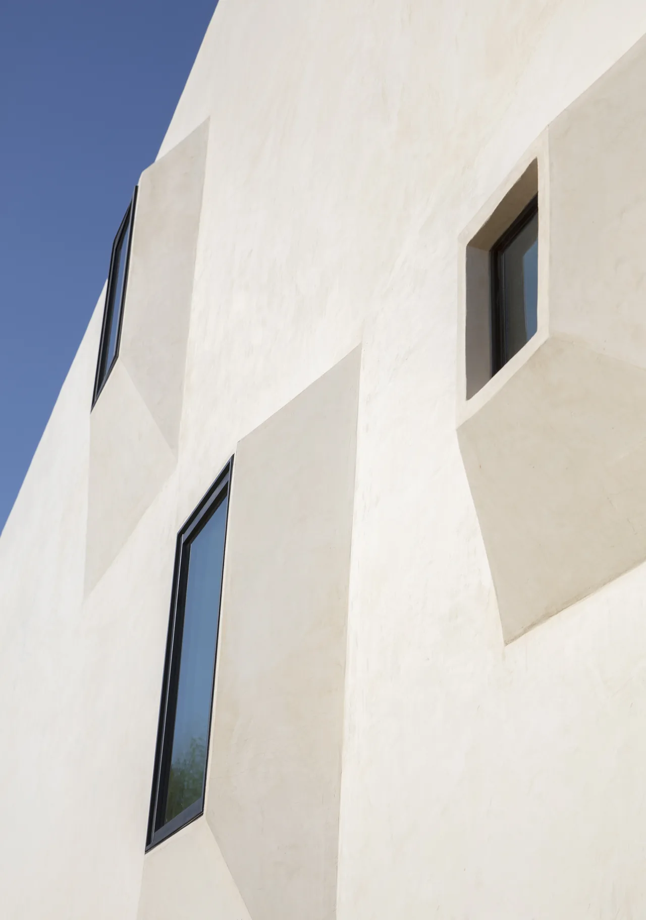 White stucco facade featuring angular deep-recessed windows with black frames creating striking shadows.