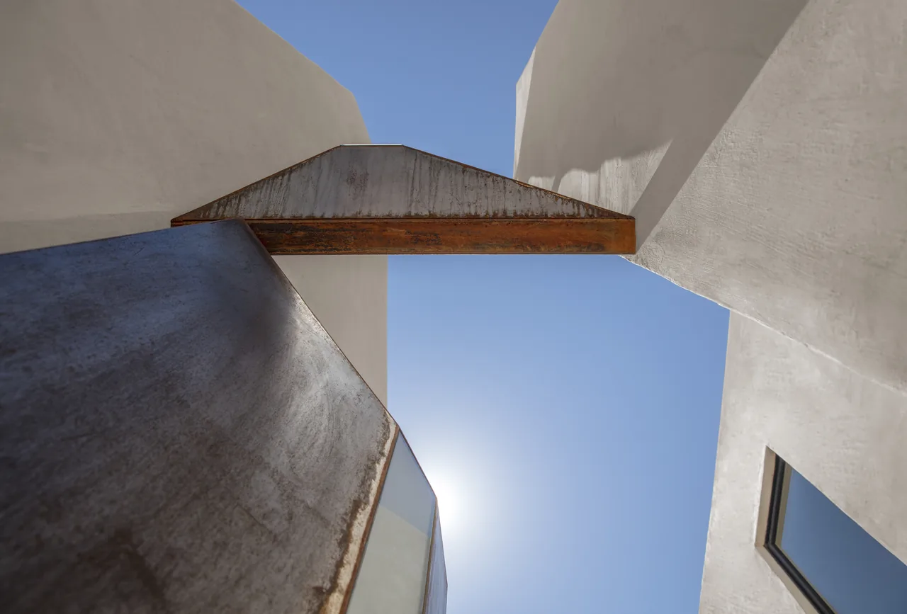 Casa Schneider features a deep recessed square sky opening framed by white stucco walls and a rusted angular metal beam.