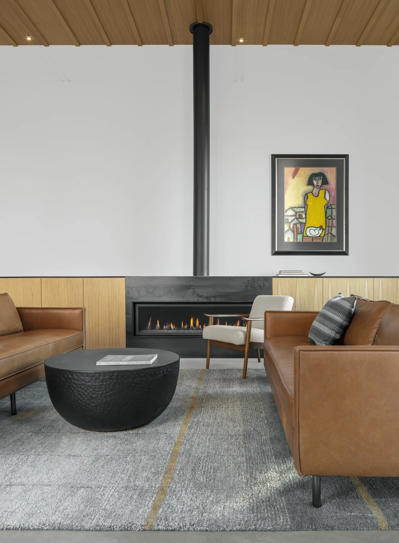 Modern living room features a linear fireplace with a tall black chimney pipe and warm wood paneling below a white wall.