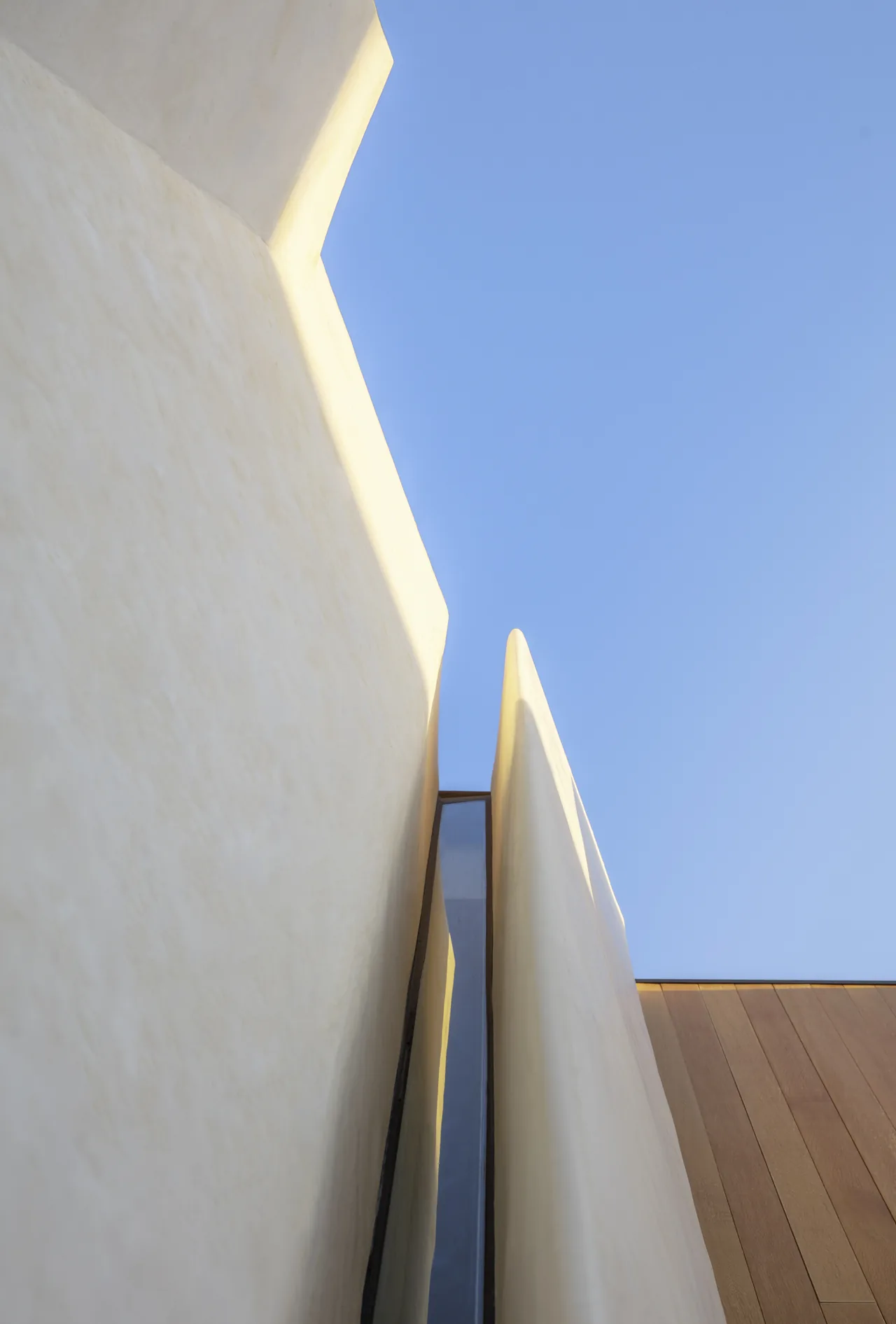 Detail of Casa Schneider showing deep recess between white stucco walls with an angular window and wood siding below.