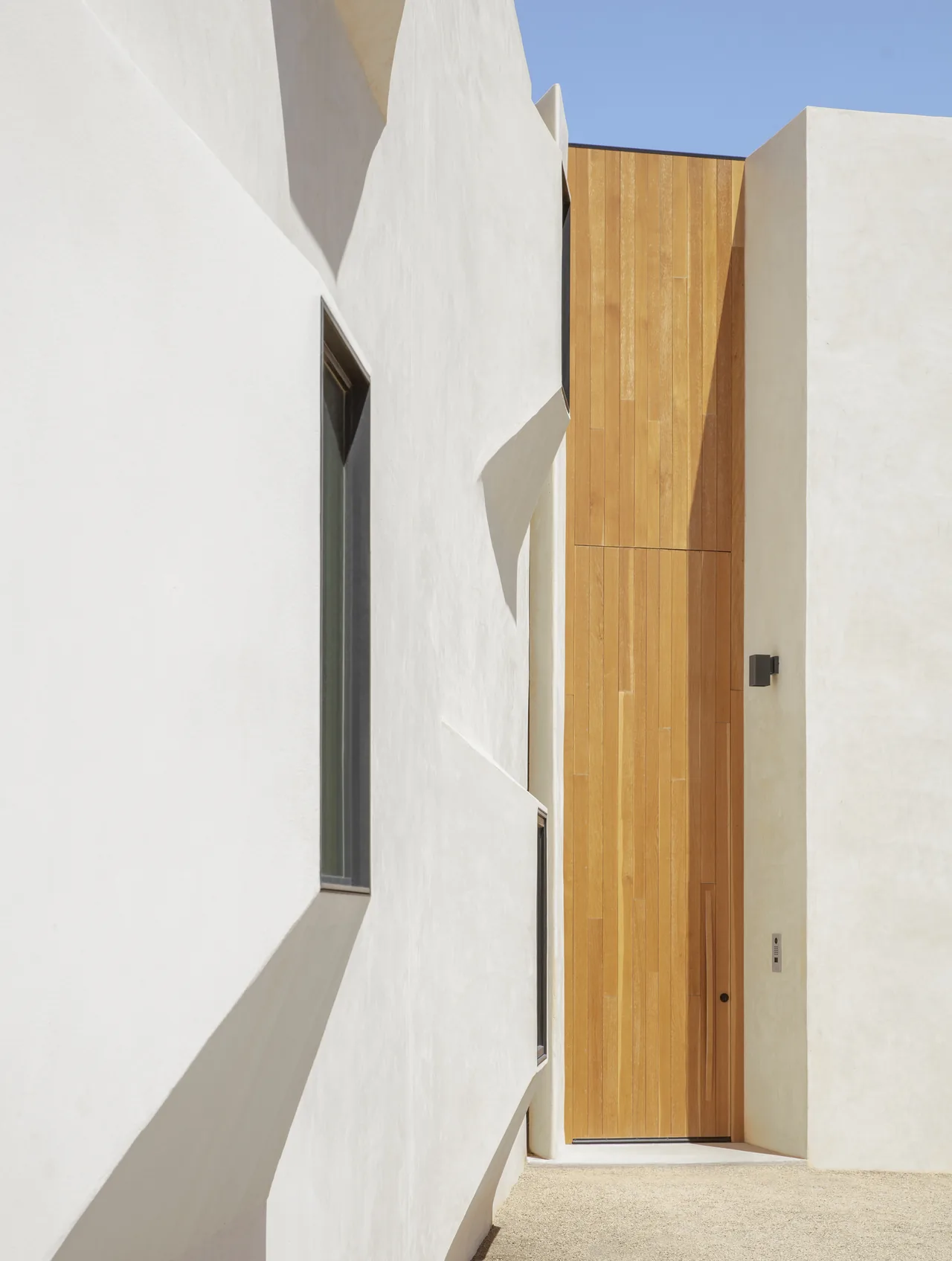 Tall wooden front door recessed into white stucco exterior walls with angular window frames at Casa Schneider.
