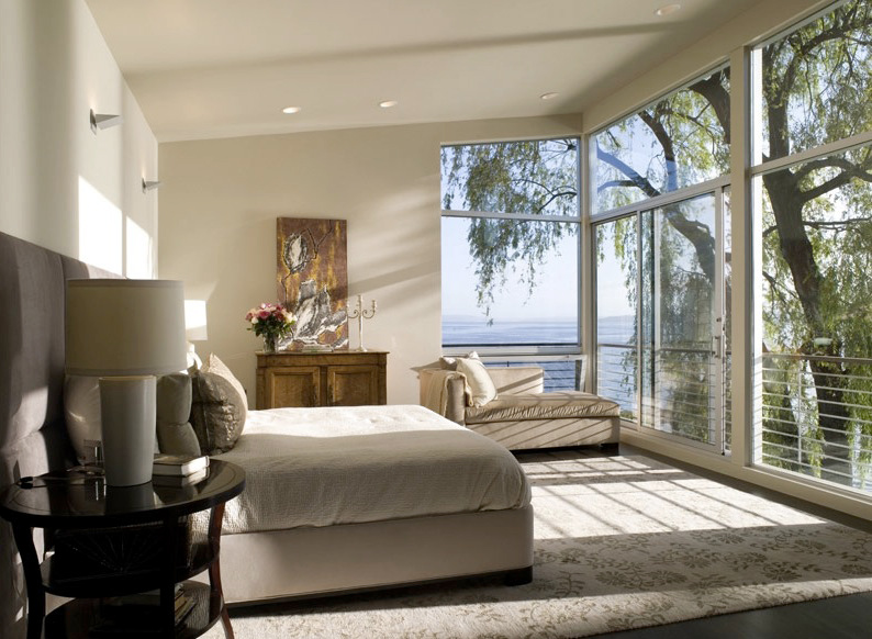Bedroom with floor-to-ceiling windows offers a view of water and trees at Leschi Lake House.