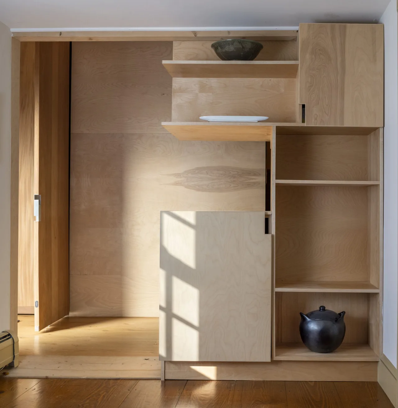 Built-in wood shelving and cabinetry features decorative pottery in a softly lit interior space of a modern addition.