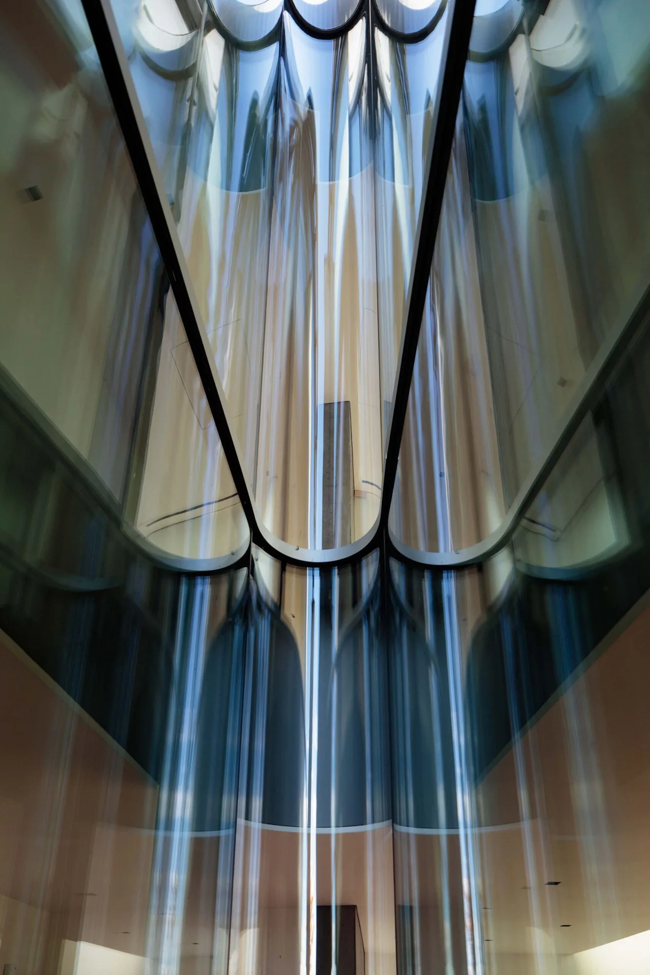 Curved glass ceiling panels create a complex reflective effect in this interior space.