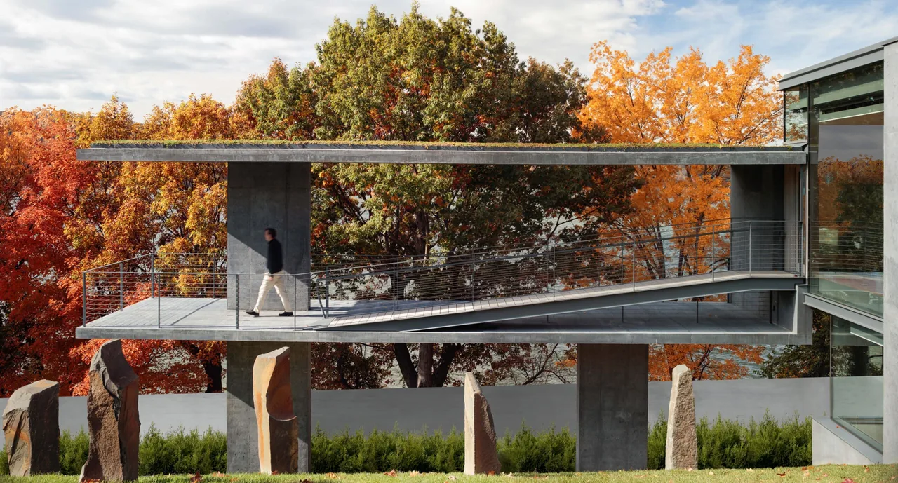 Horizon House features a concrete cantilevered walkway with stone pillars on a sloped site and views through large windows.