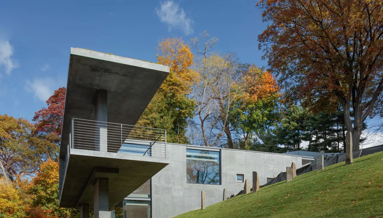 Horizon House features cantilevered concrete balconies with metal handrails on a wooded sloped site in autumn.