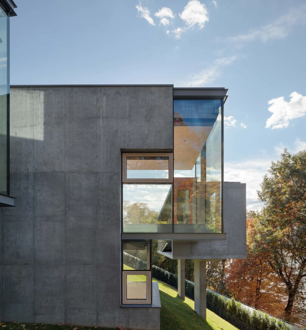 Horizon House features exposed concrete walls and a cantilevered glass section overlooking a sloped site with autumn trees.