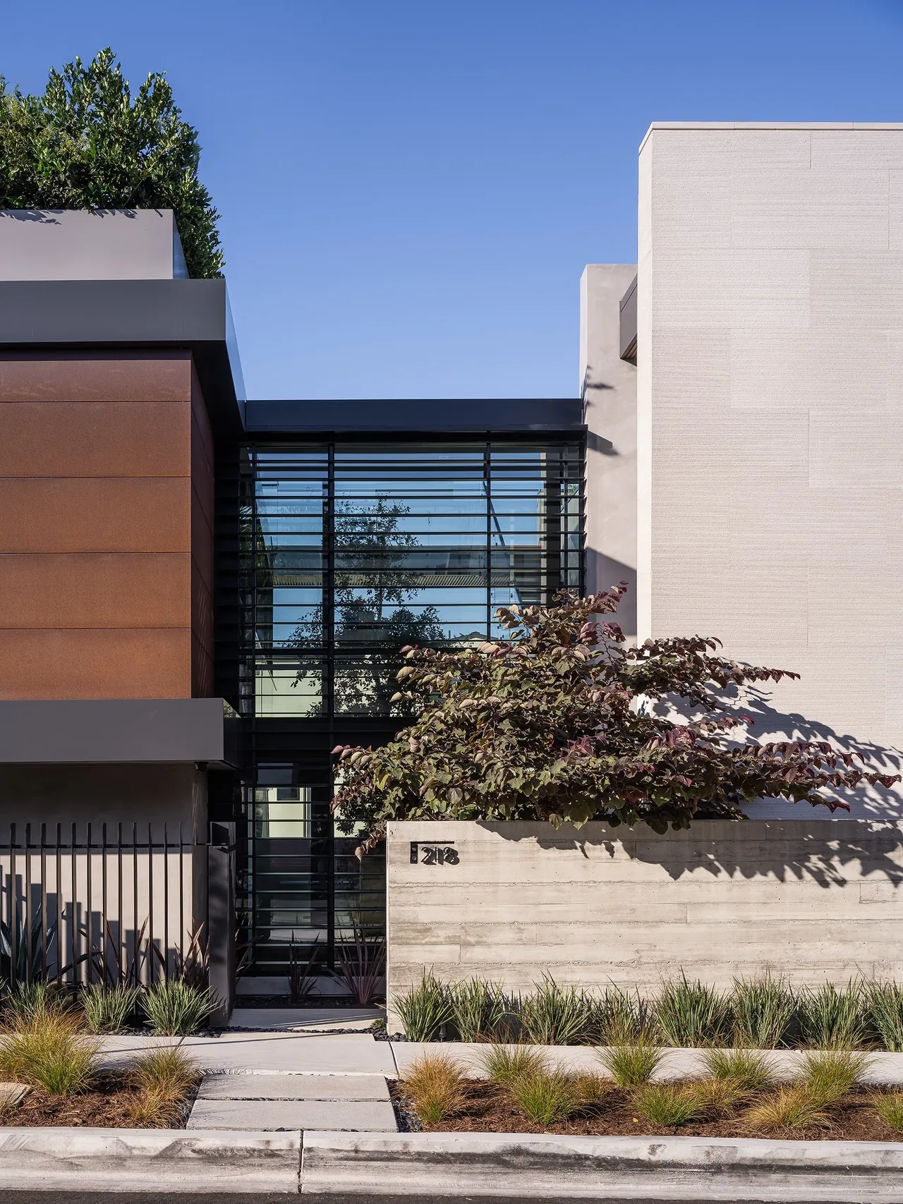Front exterior view of Goldenrod House featuring rust-colored metal panels and concrete walls with landscaped sidewalk.