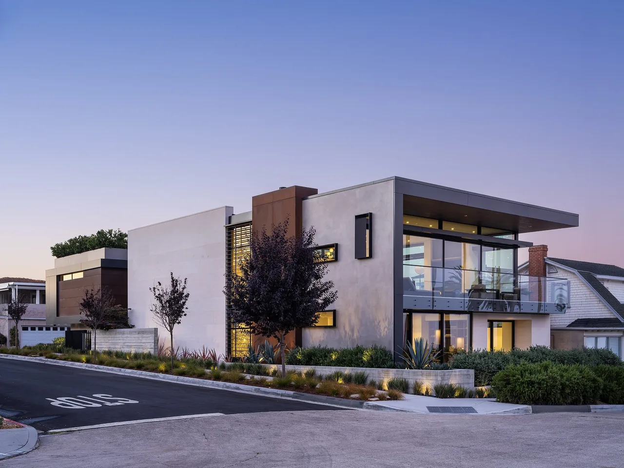 Goldenrod House features rectangular volumes, rust-colored metal panels, and a landscaped yard illuminated in evening light.