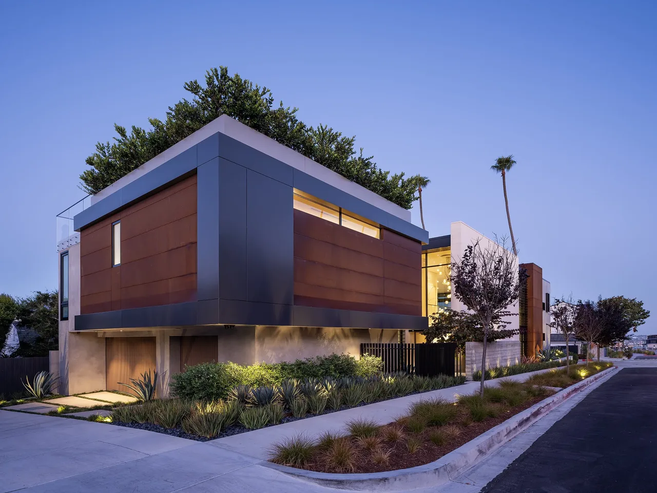 GOLDENROD HOUSE features rust-colored metal panels and a planted rooftop, capturing evening lighting in Los Angeles.