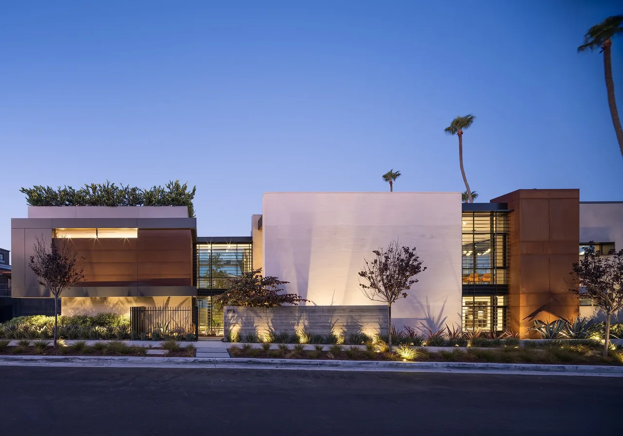 The Goldenrod House features a modern facade with glass and rust-colored metal panels, planted rooftop, and landscape lighting.