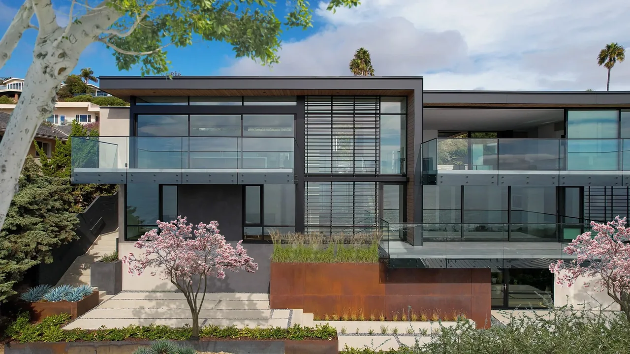 Modern two-story house with large glass windows, black frames, and rust-colored metal paneling.