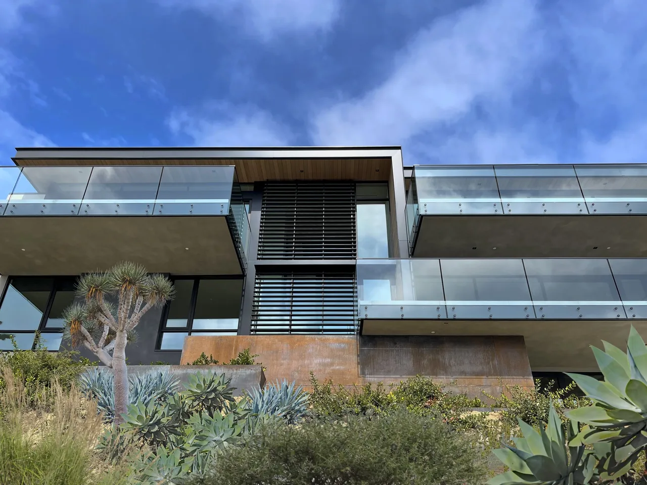 The Anacapa House features glass railing balconies and rust-colored metal paneling set against hillside landscaping.