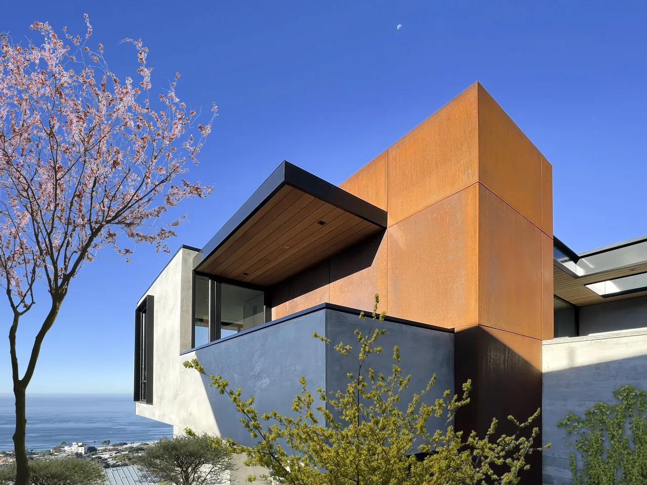 ANACAPA HOUSE features rust-colored metal panels and large windows with hillside and ocean views.