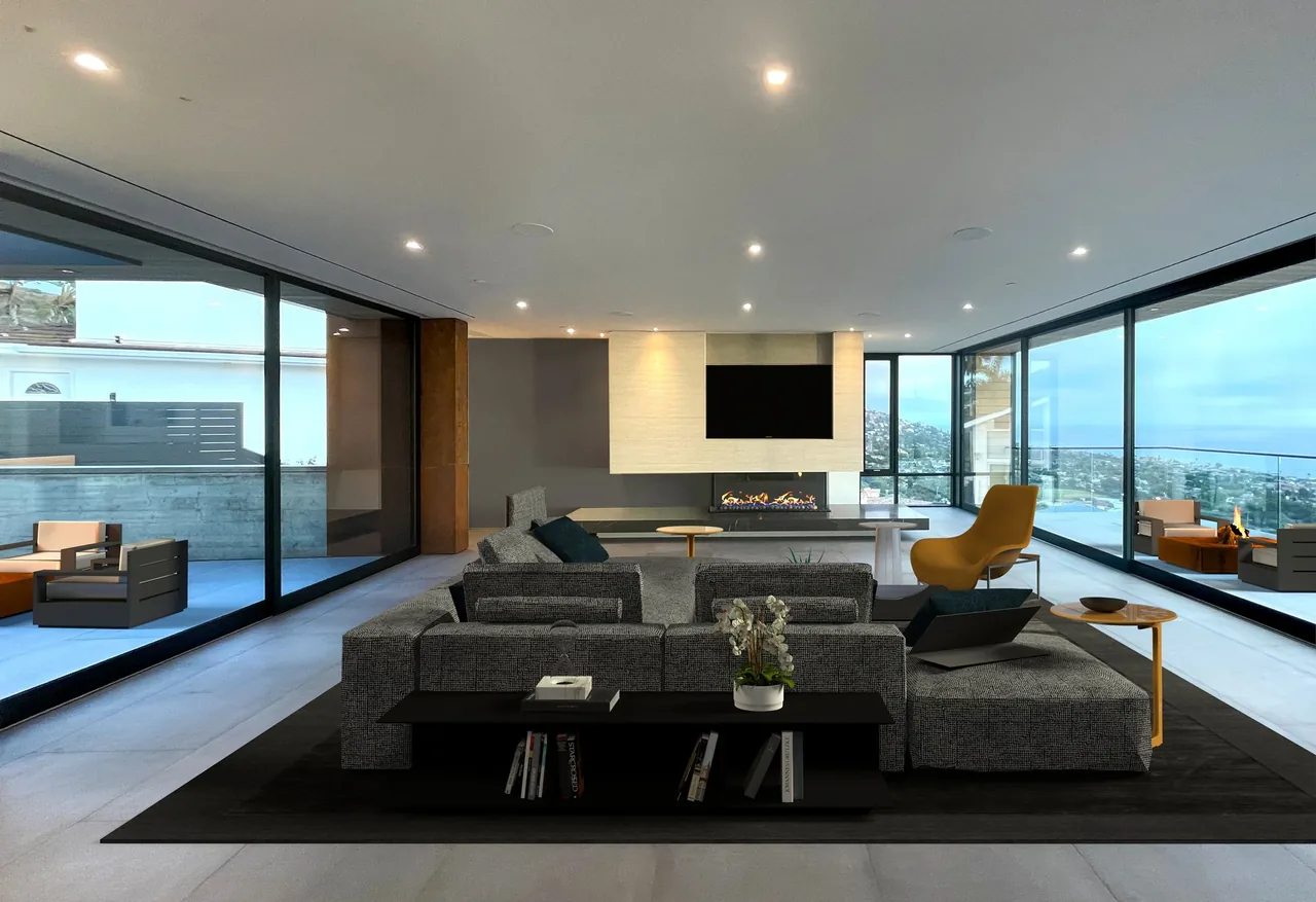 The Anacapa House living room features floor-to-ceiling windows with coastal and hillside views, a gray sectional sofa, and a linear fireplace.