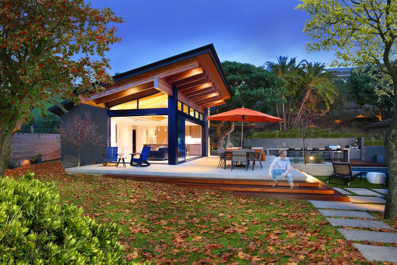 Evening view of the VOLKOV POOL HOUSE featuring wood ceiling beams and a seamless transition to outdoor living with a dining area and lounge chairs.