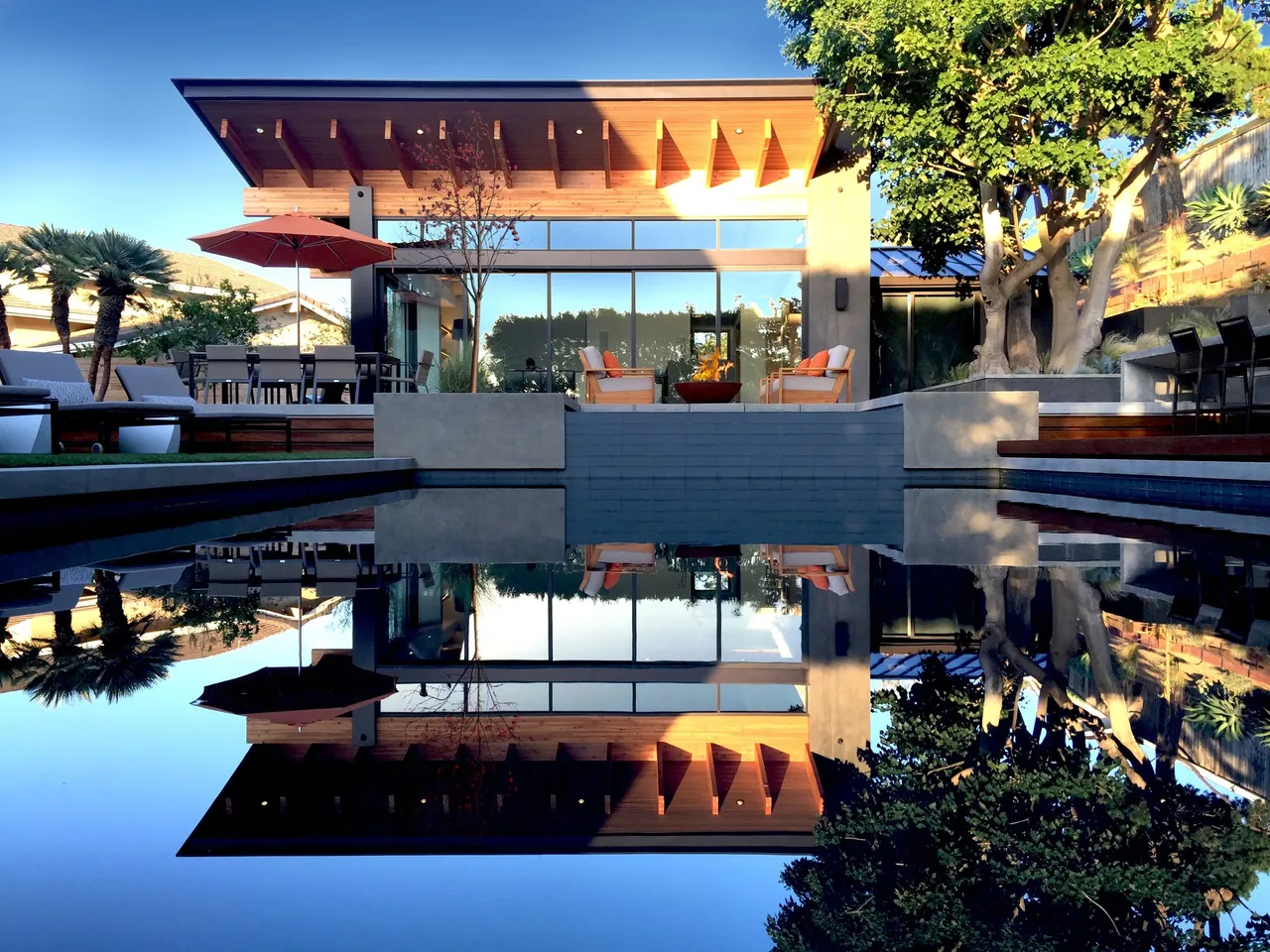 The Volkov Pool House features a flat roof with exposed beams, a reflecting pool, and an outdoor fire feature seating area.