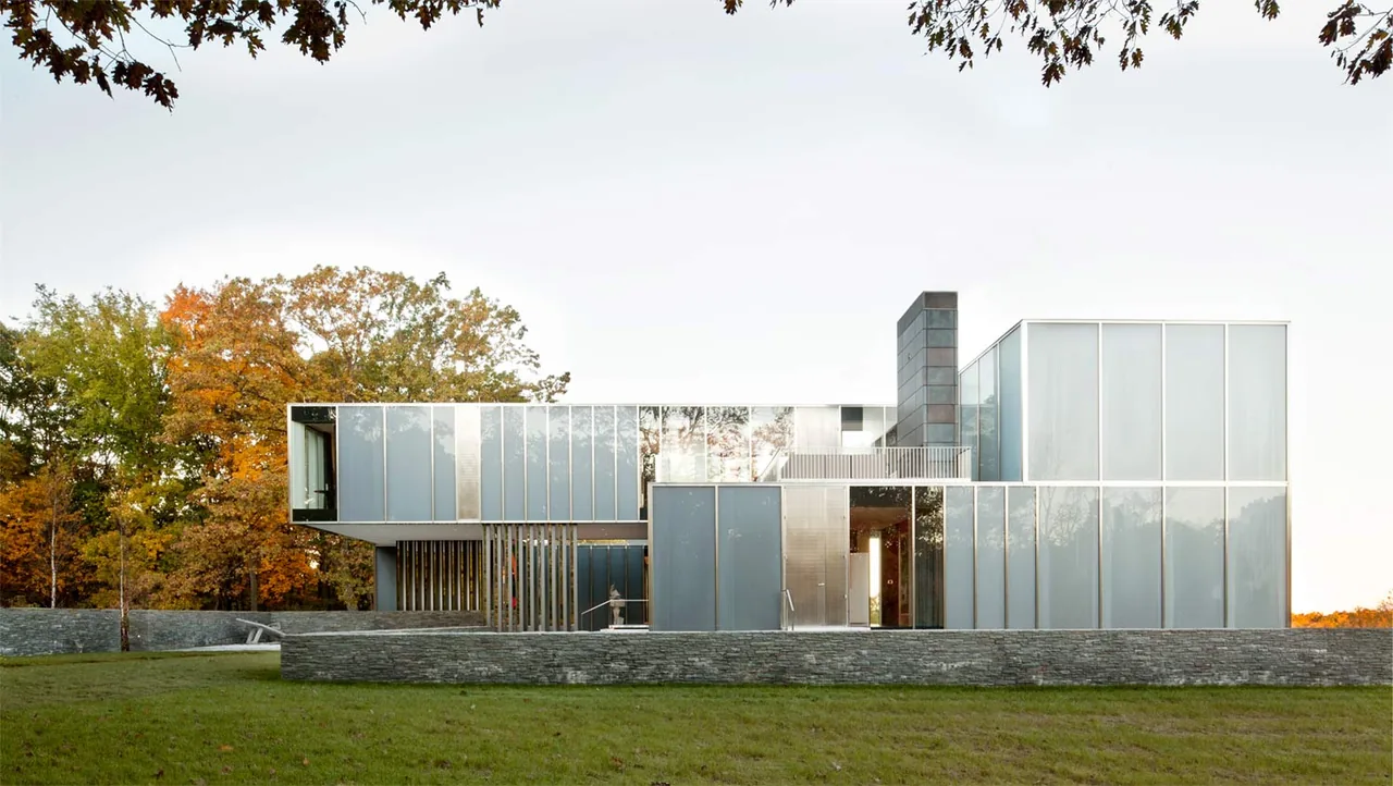 The Dutchess County Residence Main House features a modern exterior with floor-to-ceiling glazing and stone cladding, set against autumn foliage.