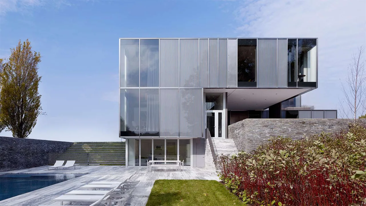 The Dutchess County Residence features large folding glass doors and a modern metal and glass facade with stone terraces around a pool.