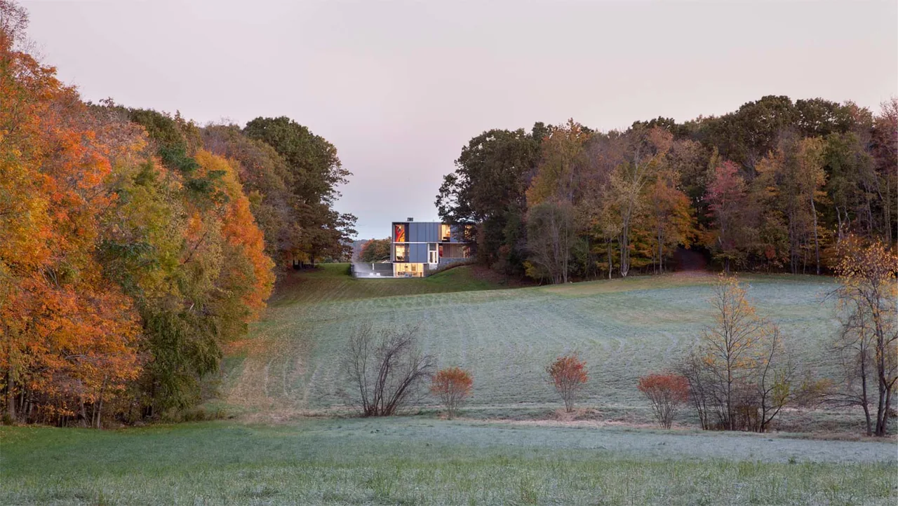 The Dutchess County Residence Main House features a modern design set within a wooded landscape with autumn colors.