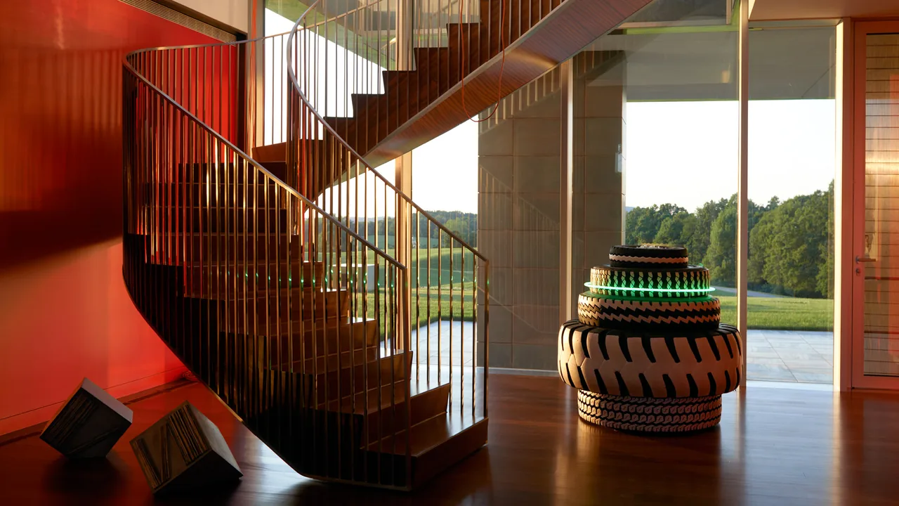 Spiral wood staircase beside large glass window with a stacked circular sculpture near the entry of Dutchess County Residence.